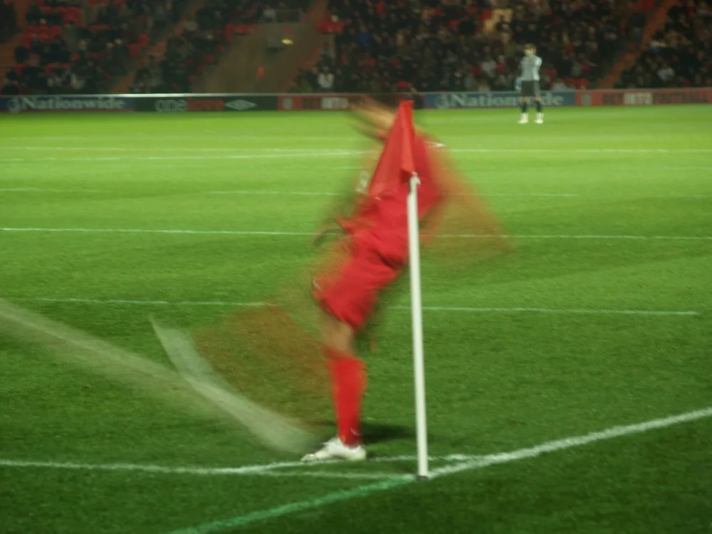 Close up shot of a football placed at the corner kick spot on a green football p