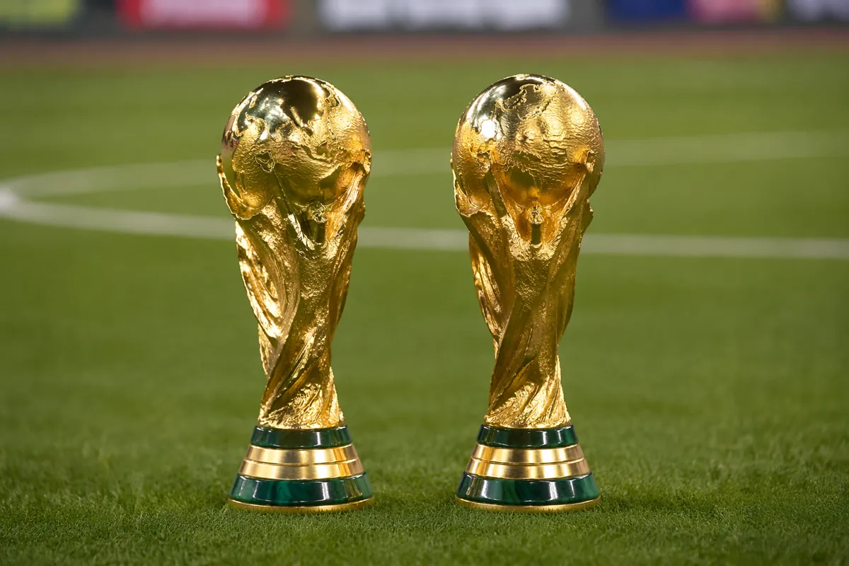 Two classic FIFA World Cup trophy replicas placed side by side on a well-maintained green