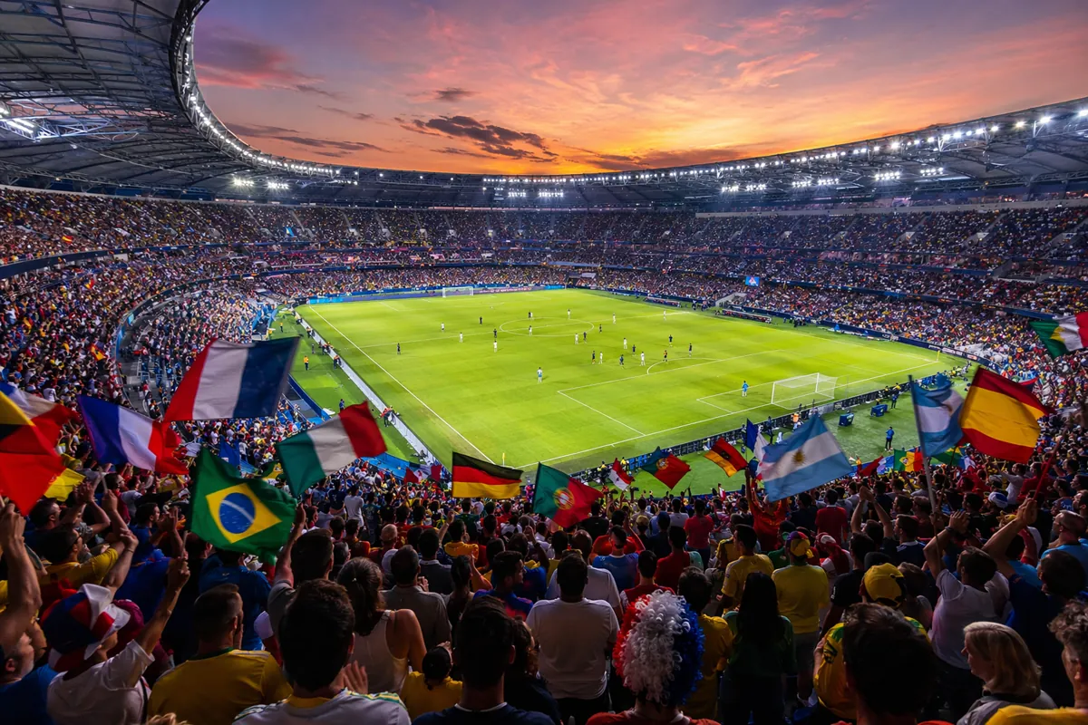 Wide shot of a packed World Cup football stadium at dusk, colorful fans waving national fl